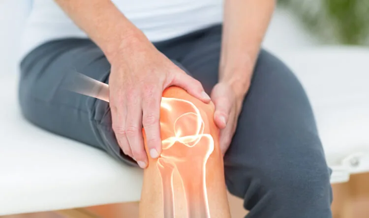 A person holding their knee with a glowing joint illustration, symbolizing the need for supplements for bone and joint health.