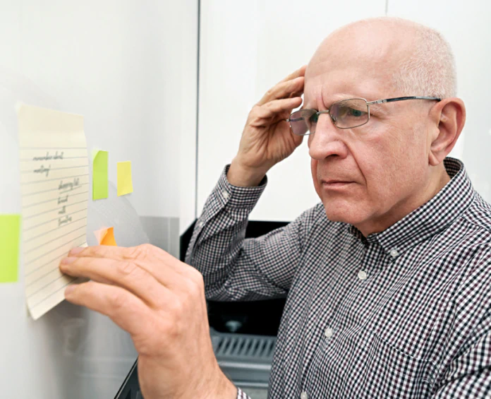 An elderly man looking at notes on a fridge, representing the importance of brain and mental health supplements for memory and focus.