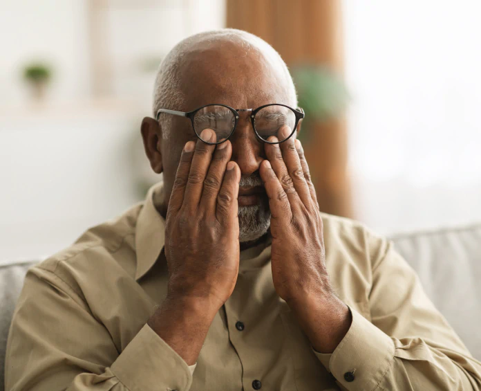 A tired man rubbing his eyes while sitting on a couch, highlighting the need for energy supplements to combat fatigue.