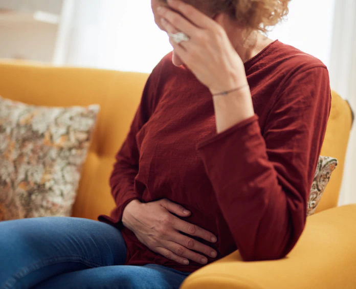 A woman sitting on a couch holding her stomach, highlighting the benefits of gut health and digestion supplements.