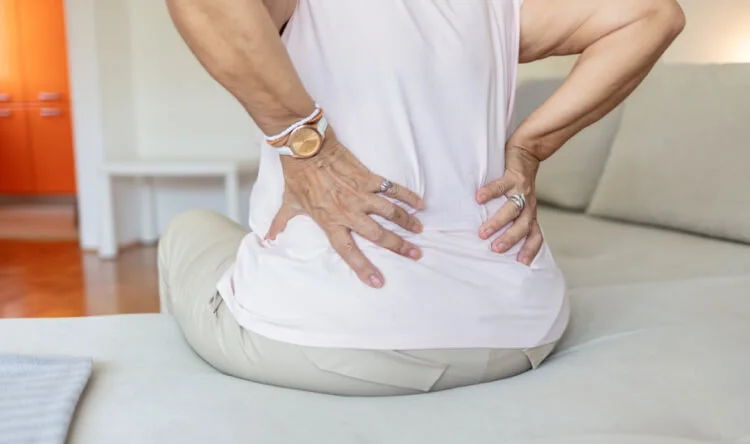 A woman sitting on a couch holding her lower back, representing the need for supplements for kidney health.