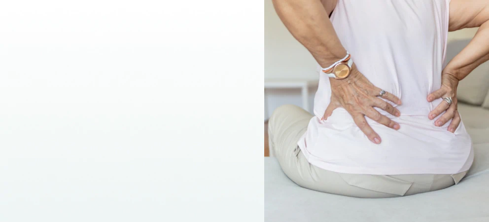A woman sitting on a couch holding her lower back, representing the need for supplements for kidney health.