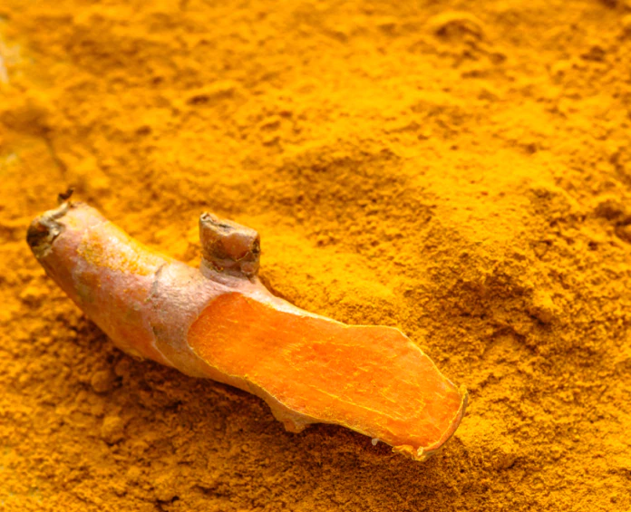 A sliced turmeric root on a pile of bright yellow turmeric powder, commonly used in liver health supplements for its beneficial properties.
