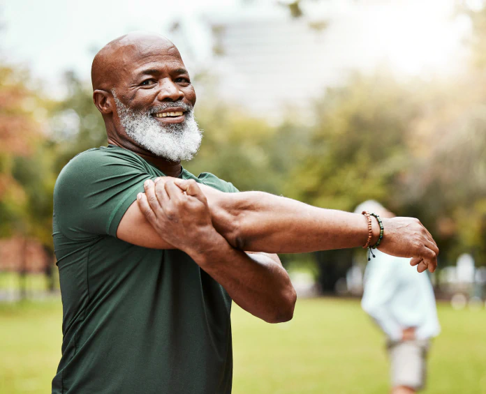 A fit older man stretching his arms in a park, maintaining wellness with optimal health supplements for daily vitality.