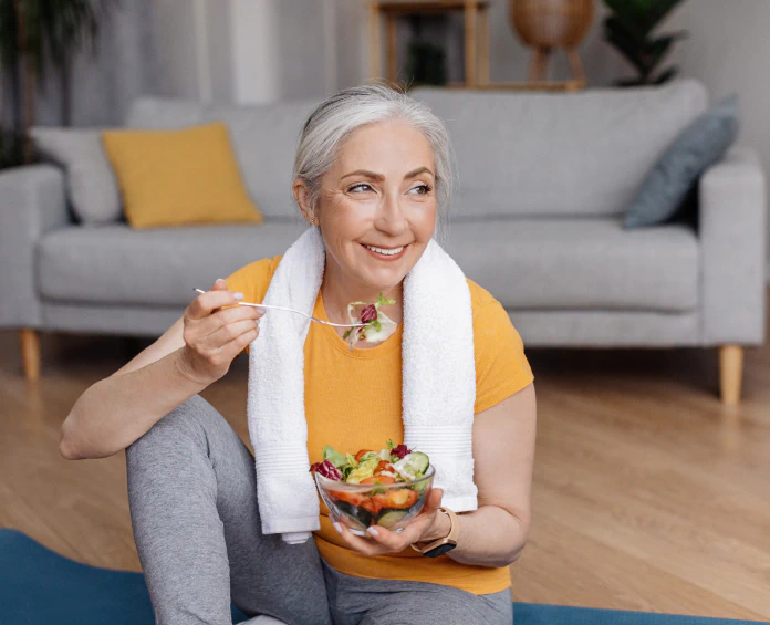 A happy older woman eating a fresh salad at home after a workout, focusing on nutrition and the best supplements for optimal health.