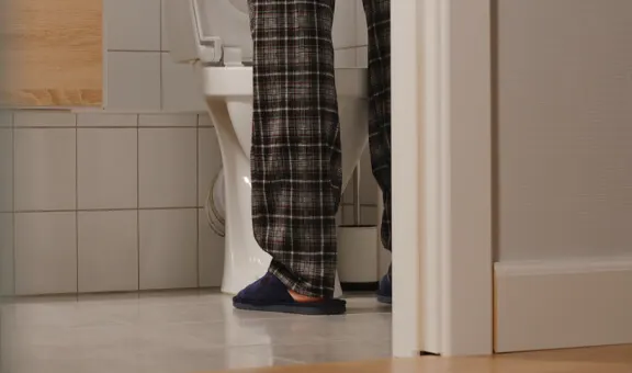 A middle-aged man in pajamas standing in a bathroom at night, symbolizing frequent urination and the need for supplements for prostate health.