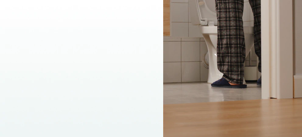 A middle-aged man in pajamas standing in a bathroom at night, symbolizing frequent urination and the need for supplements for prostate health.