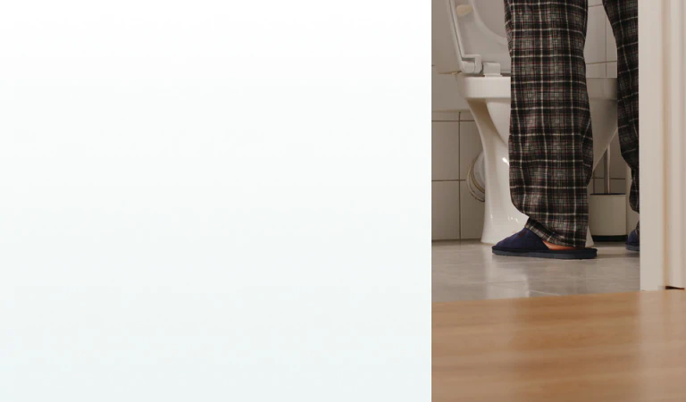 A middle-aged man in pajamas standing in a bathroom at night, symbolizing frequent urination and the need for supplements for prostate health.