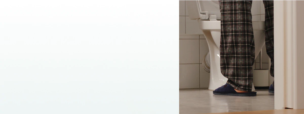 A middle-aged man in pajamas standing in a bathroom at night, symbolizing frequent urination and the need for supplements for prostate health.