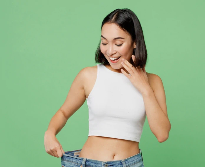 A happy woman in a white top looking at her loose jeans, celebrating success with the best supplements for weight loss.
