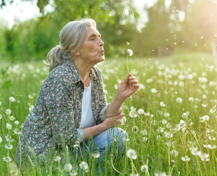 A senior woman in a meadow blowing a dandelion, embodying wellness and freedom supported by the best supplements for women's health.